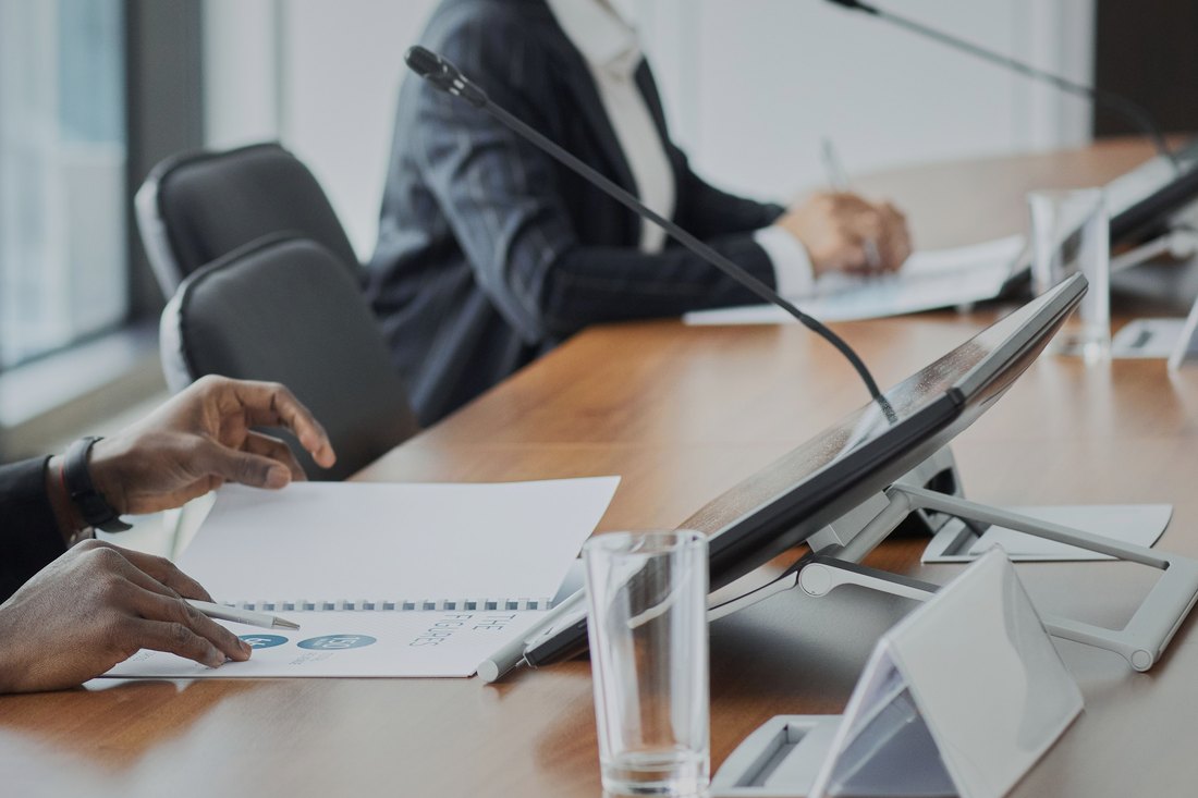 Two people working at a boardroom table with microphones and a report