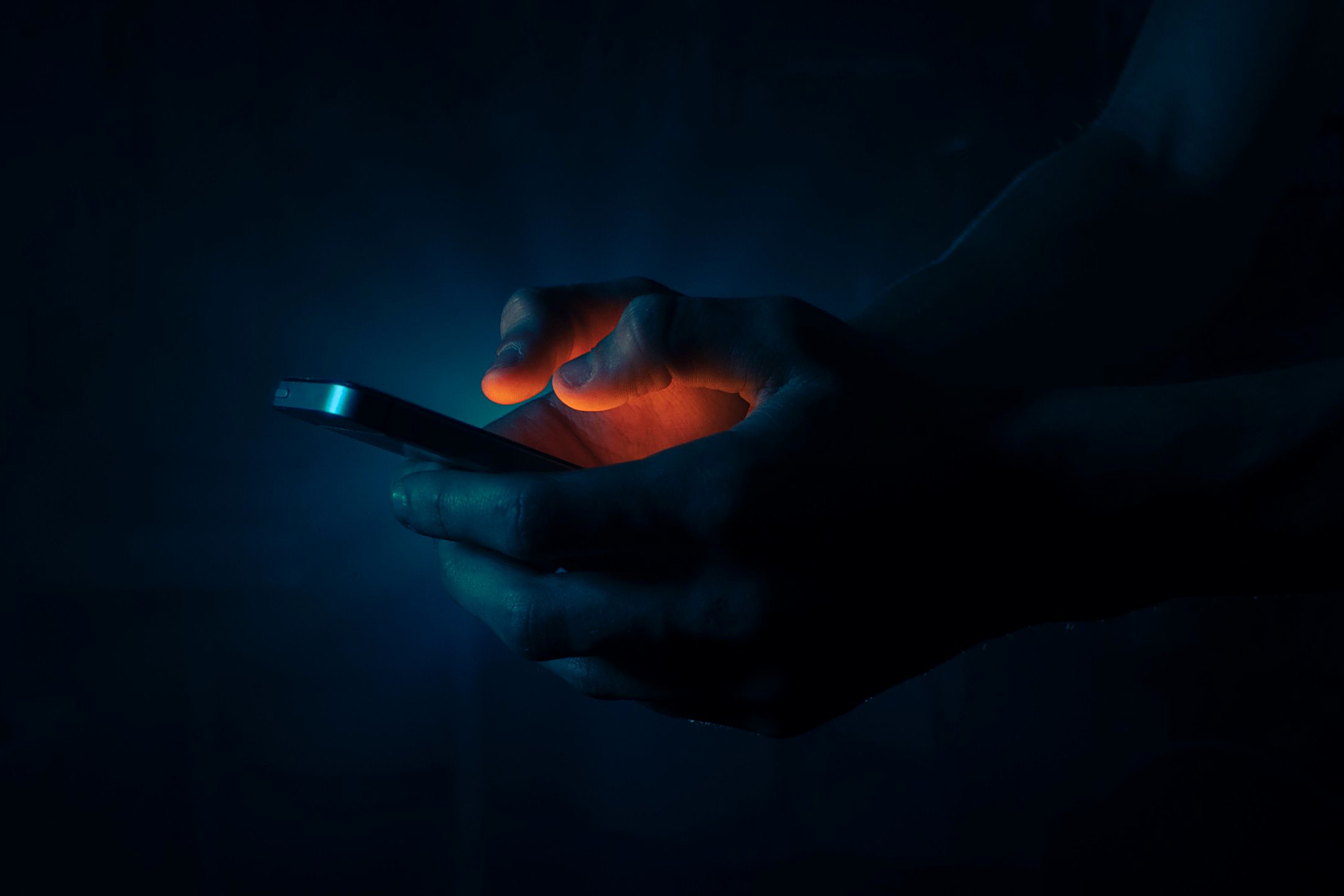 A hand using a smartphone in the dark, lit by the screen