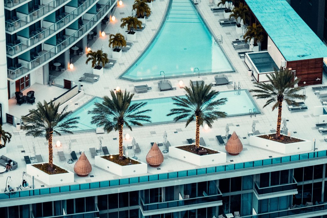 Aerial view of a rooftop pool deck with palm trees between high-rise residential towers
