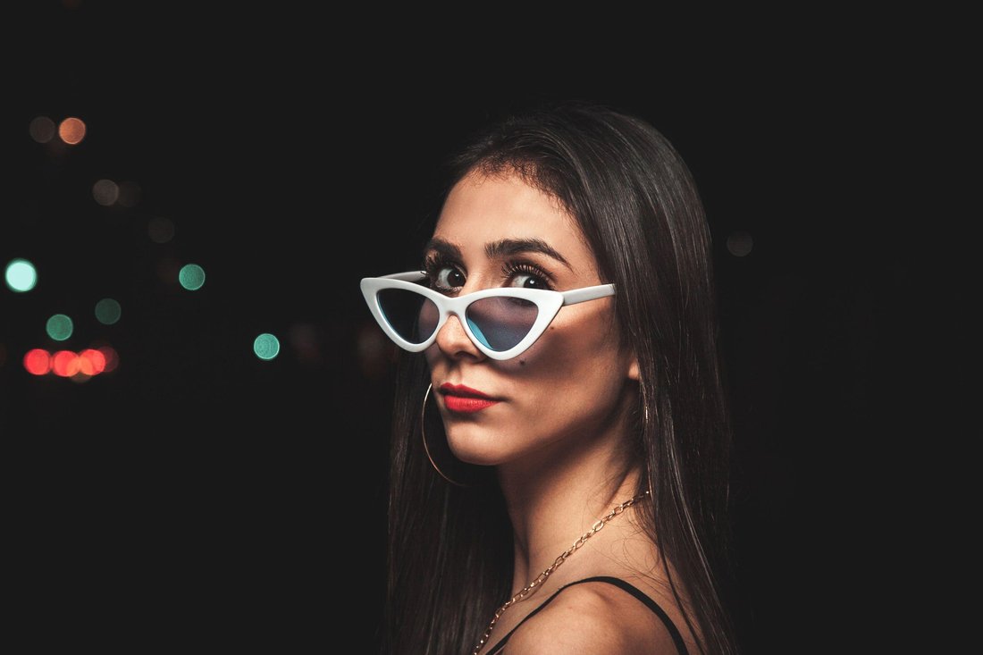 A woman in white cat-eye sunglasses against city lights at night