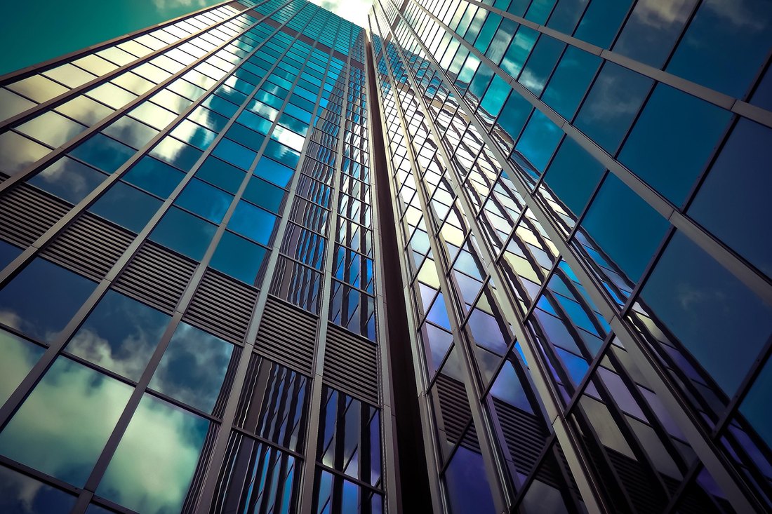 Looking up a glass office tower reflecting blue sky and clouds